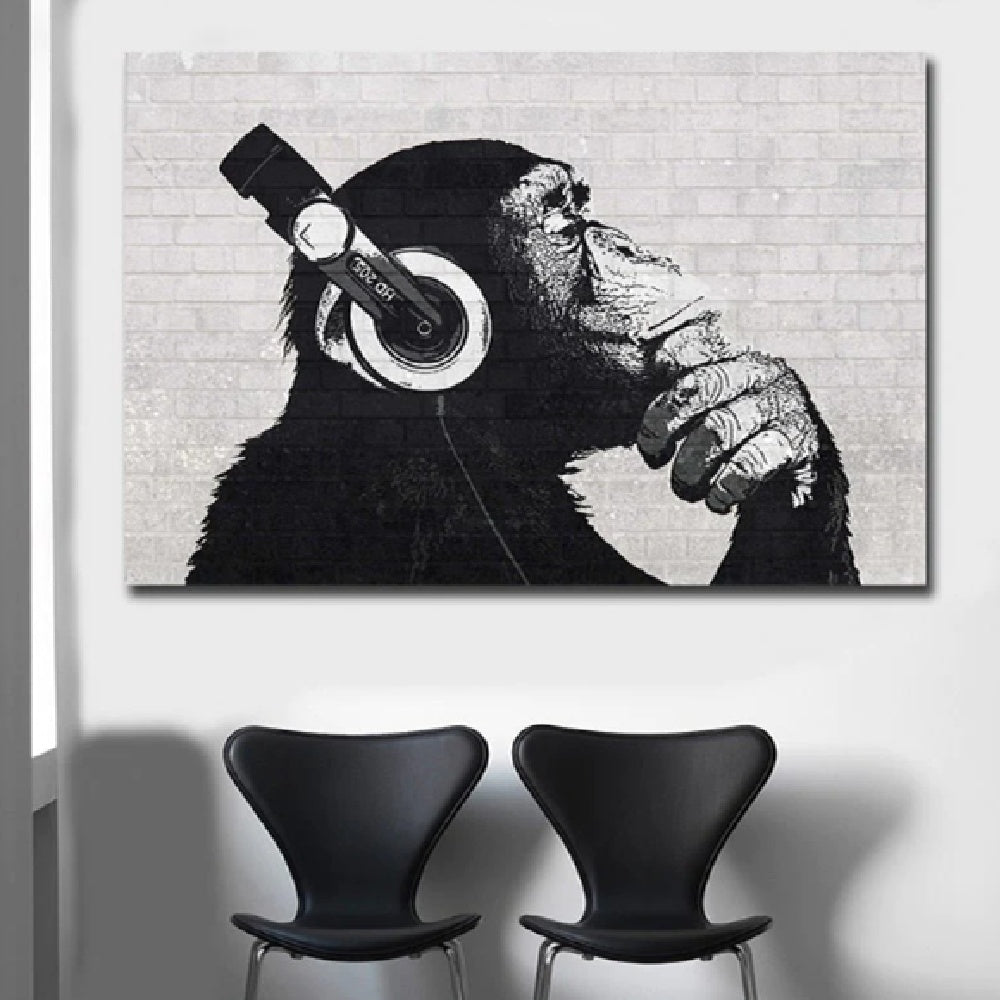 Canvas print of a chimpanzee wearing headphones against a brick wall with two black chairs below.