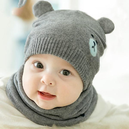 Baby wearing a gray knit hat with bear ears and a matching scarf on a white background