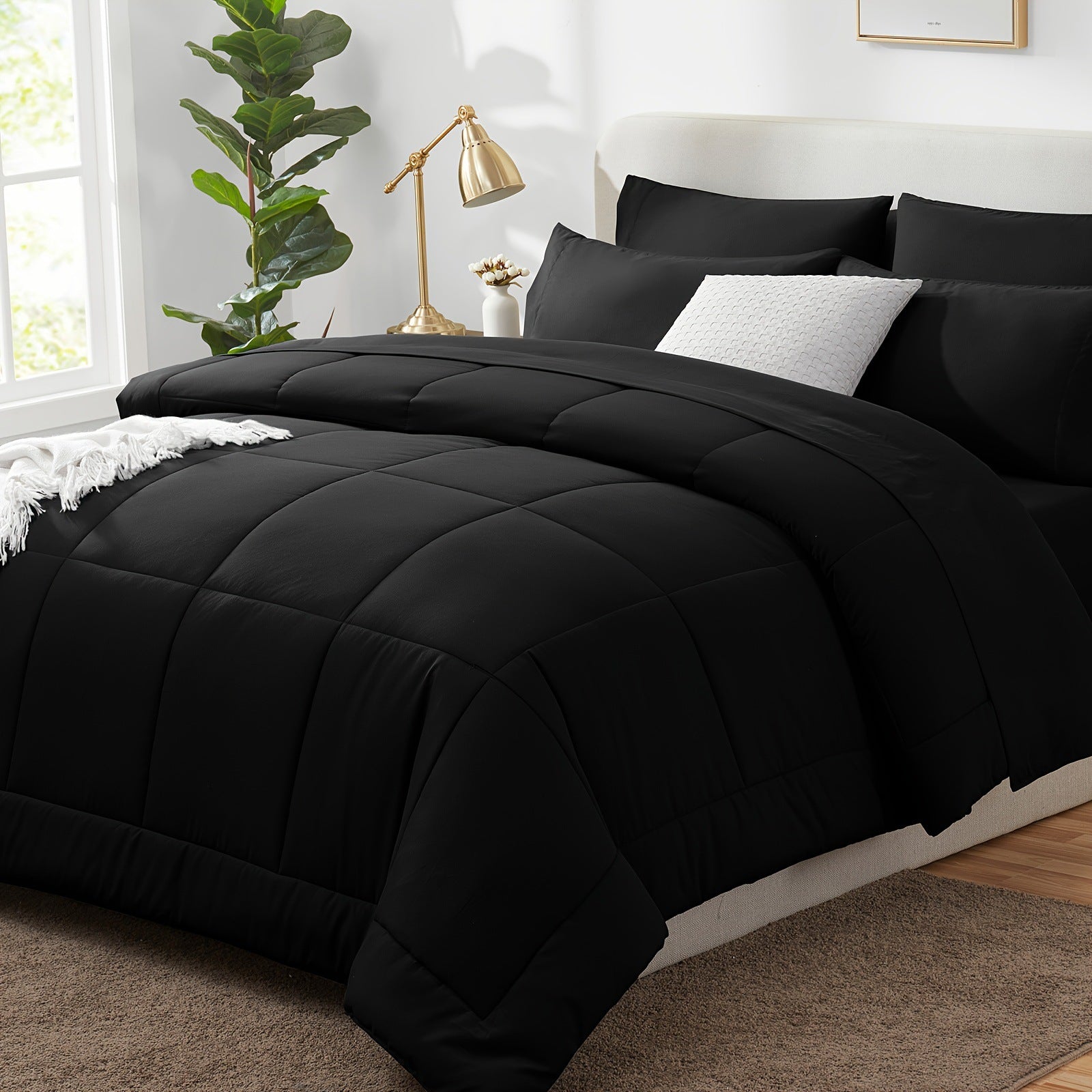 Black quilted comforter set on a bed in a bedroom with a lamp and plant.