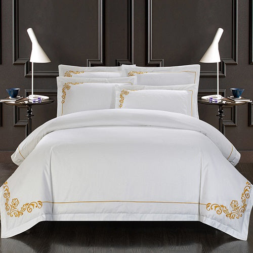 White bedding set with gold embroidery on a bed in a bedroom setting.