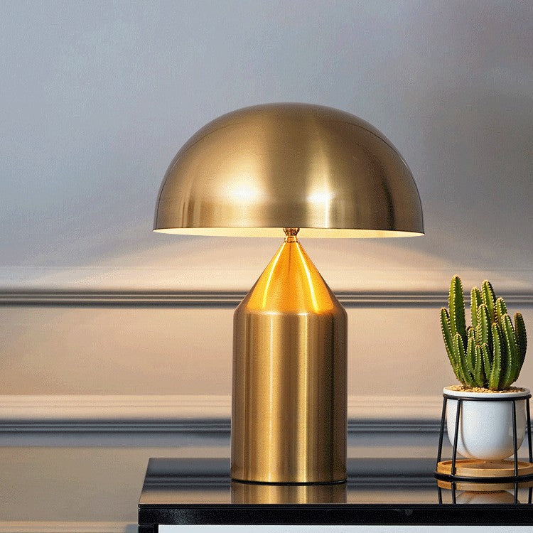 Gold table lamp on a surface with a cactus plant in the background