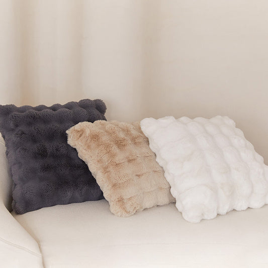 Three textured pillows in black, beige, and white on a light-colored sofa.