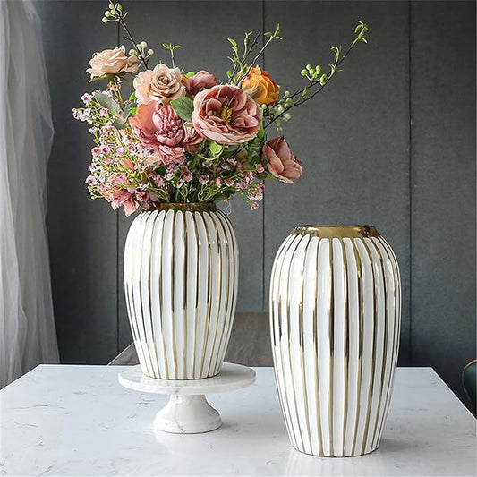 Two decorative vases with floral arrangements on a marble surface against a gray wall.